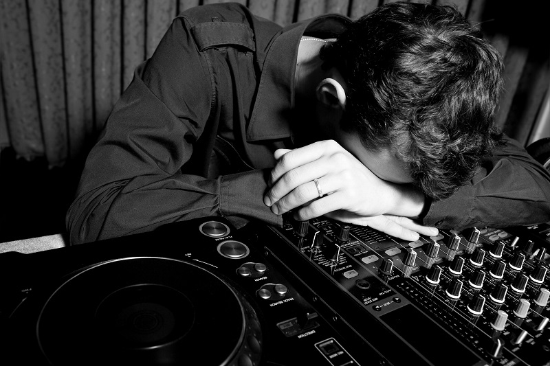 Tired DJ resting on a mixer, illustrating the risk of hiring an unprofessional cheap wedding DJ